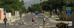 Wide paved path with roundabout in center. Surrounded by trees on both sides. Along the path are street signs indicating this is a bike boulevard and the direction of traffic. 
