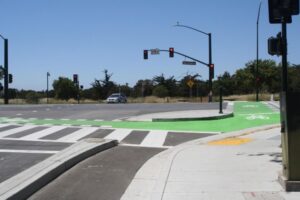Multi-lane street of intersection. Bike lane on the right side with cement curb barricade between cars and bikers. 