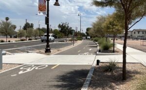 A street that features multiple parallel means of transportation. To the left is two lanes for cars, in the middle is double lane bike path, and to on the right is a sidewalk for pedestrians. 